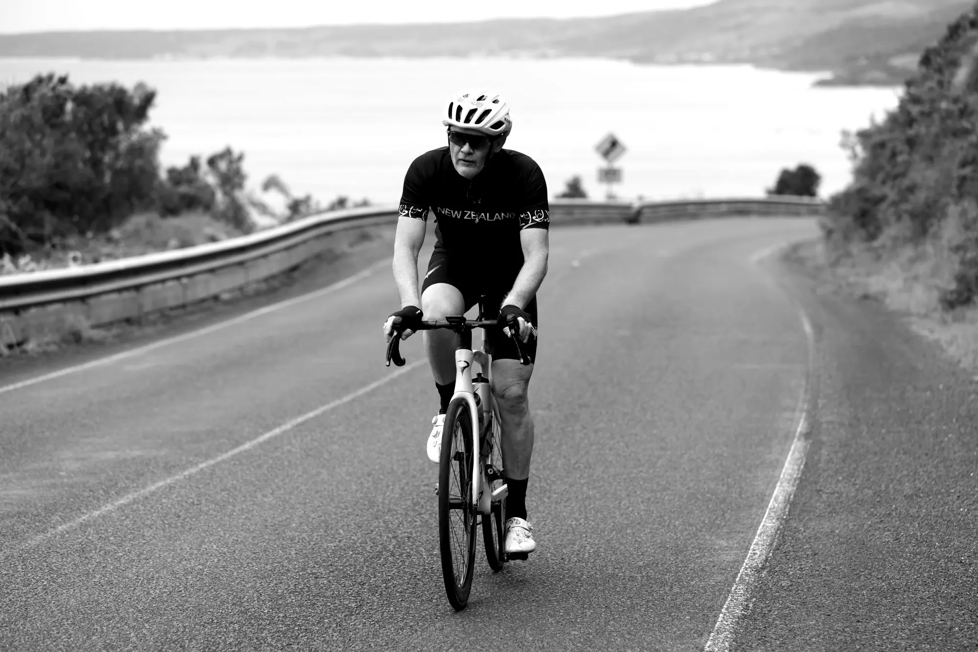 Black and white photograph of a cyclist riding down a country road